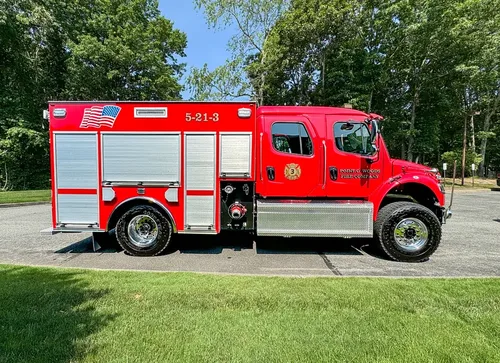 Exterior view of small fire truck showing cab, body compartments, and wheel/tire area.