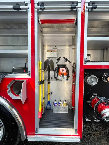 Exterior view of small fire truck showing cab, body compartments, and wheel/tire area.