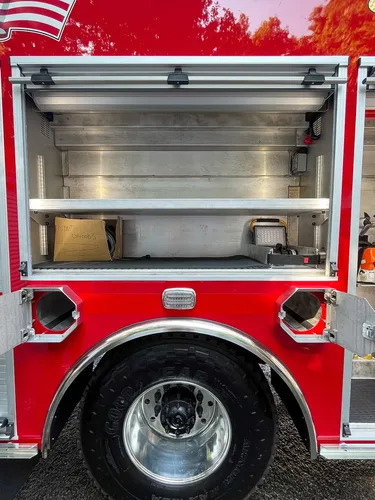 Exterior view of small fire truck showing cab, body compartments, and wheel/tire area.