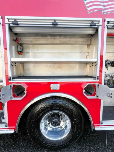 Exterior view of small fire truck showing cab, body compartments, and wheel/tire area.