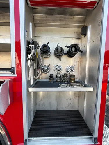 Exterior view of small fire truck showing cab, body compartments, and wheel/tire area.