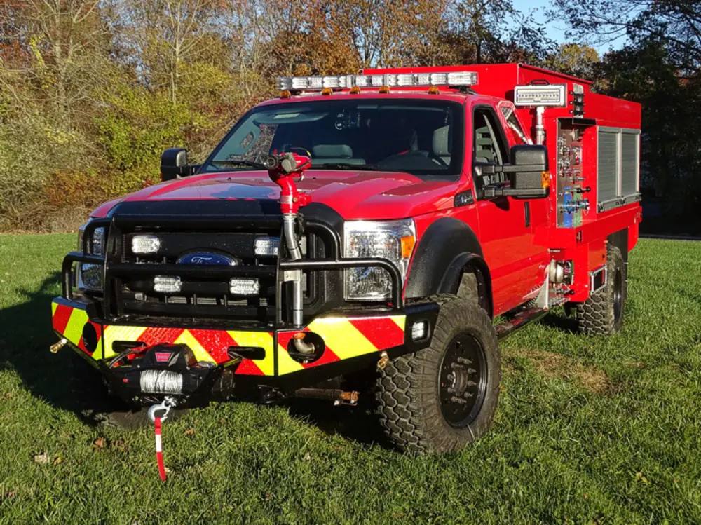 Exterior view of small fire truck showing cab, body compartments, and wheel/tire area.