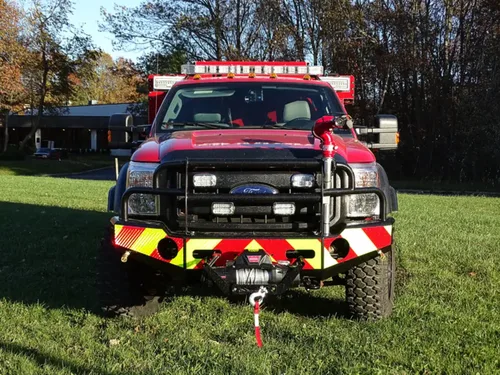 Exterior view of small fire truck showing cab, body compartments, and wheel/tire area.