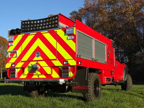 Exterior view of small fire truck showing cab, body compartments, and wheel/tire area.