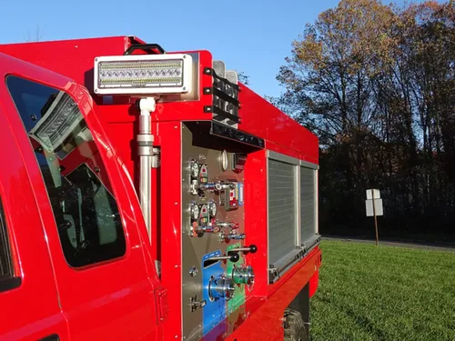 Exterior view of small fire truck showing cab, body compartments, and wheel/tire area.