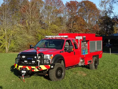 Exterior view of small fire truck showing cab, body compartments, and wheel/tire area.