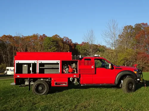 Exterior view of small fire truck showing cab, body compartments, and wheel/tire area.