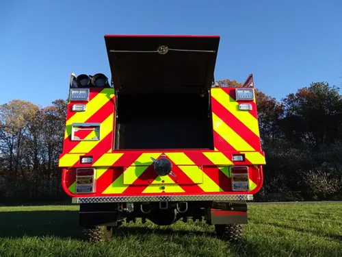 Exterior view of small fire truck showing cab, body compartments, and wheel/tire area.