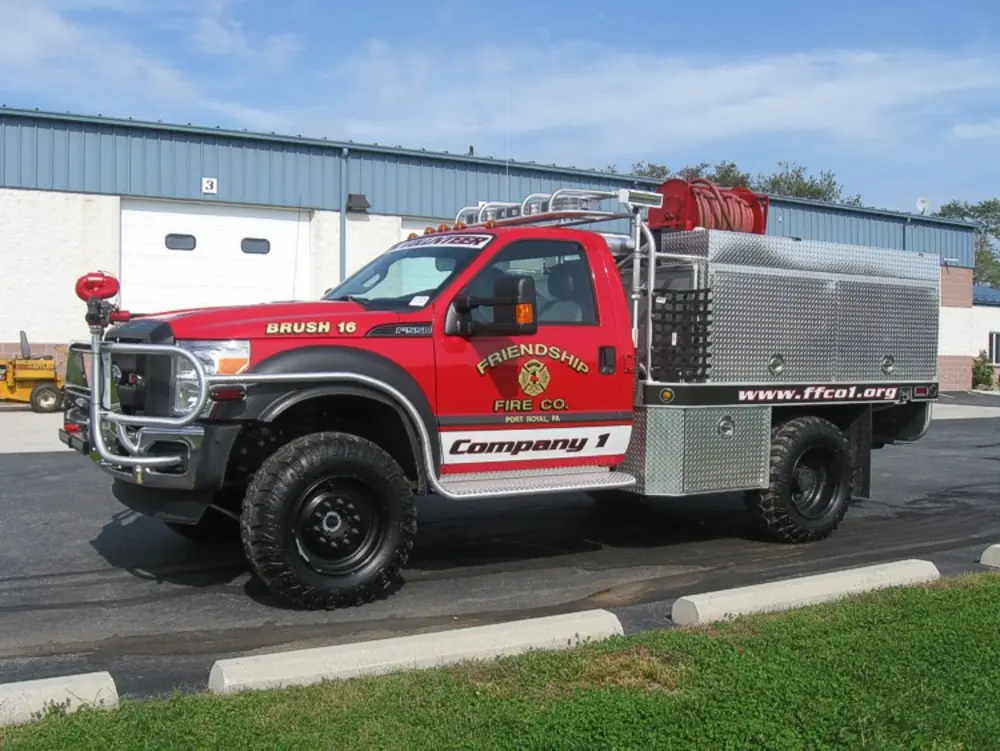Exterior view of small fire truck showing cab, body compartments, and wheel/tire area.