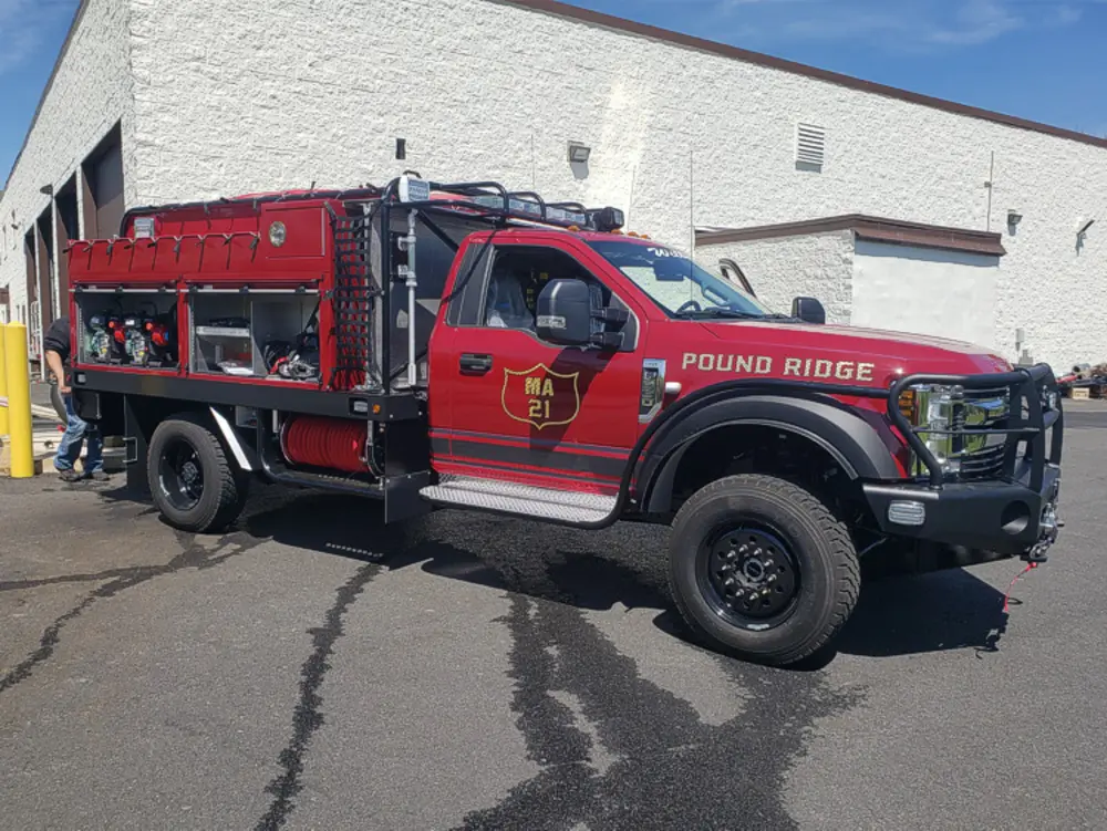 Exterior view of small fire truck showing cab, body compartments, and wheel/tire area.