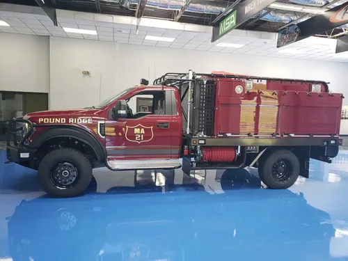 Exterior view of small fire truck showing cab, body compartments, and wheel/tire area.