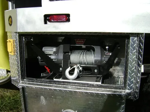Exterior view of small fire truck showing cab, body compartments, and wheel/tire area.
