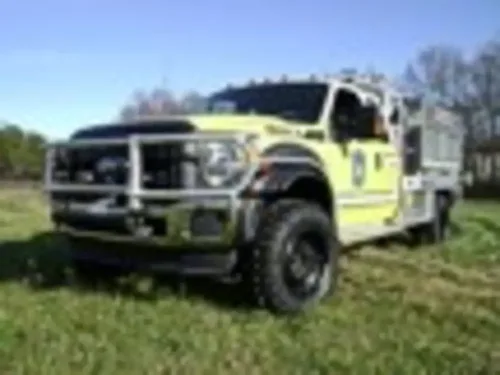 Exterior view of small fire truck showing cab, body compartments, and wheel/tire area.