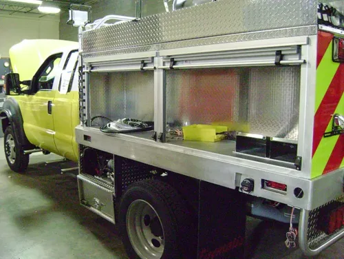 Exterior view of small fire truck showing cab, body compartments, and wheel/tire area.