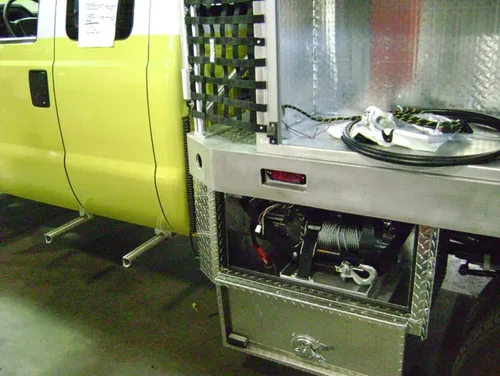 Exterior view of small fire truck showing cab, body compartments, and wheel/tire area.