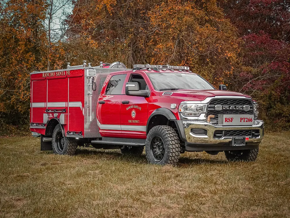 Exterior view of small fire truck showing cab, body compartments, and wheel/tire area.