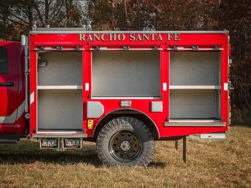 Exterior view of small fire truck showing cab, body compartments, and wheel/tire area.
