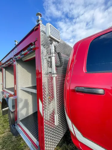 Exterior view of small fire truck showing cab, body compartments, and wheel/tire area.