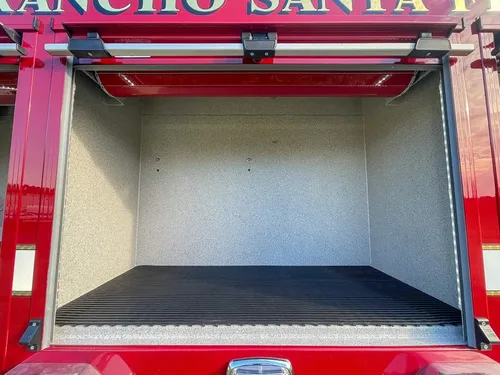 Exterior view of small fire truck showing cab, body compartments, and wheel/tire area.