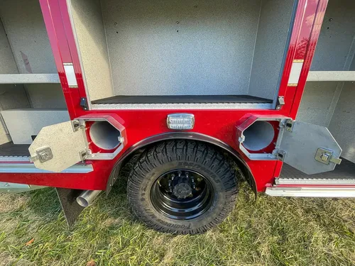 Exterior view of small fire truck showing cab, body compartments, and wheel/tire area.
