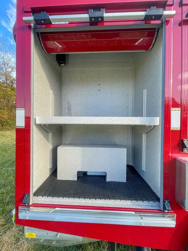 Exterior view of small fire truck showing cab, body compartments, and wheel/tire area.