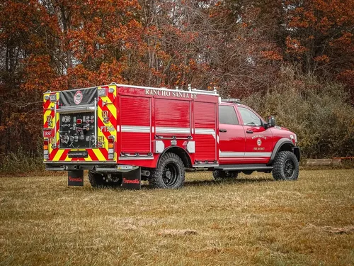 Exterior view of small fire truck showing cab, body compartments, and wheel/tire area.