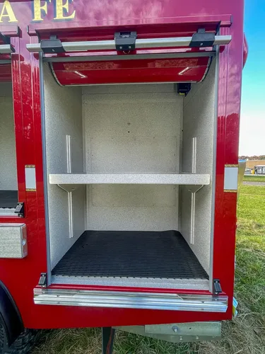 Exterior view of small fire truck showing cab, body compartments, and wheel/tire area.