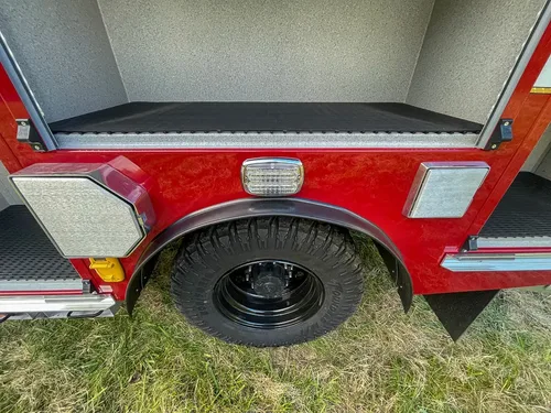 Exterior view of small fire truck showing cab, body compartments, and wheel/tire area.