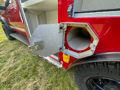 Exterior view of small fire truck showing cab, body compartments, and wheel/tire area.