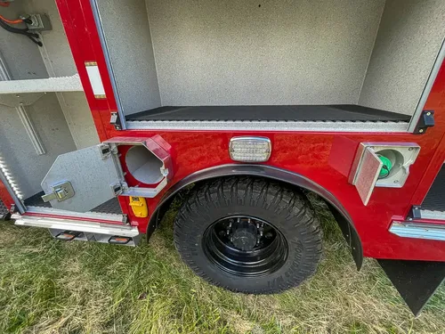 Exterior view of small fire truck showing cab, body compartments, and wheel/tire area.