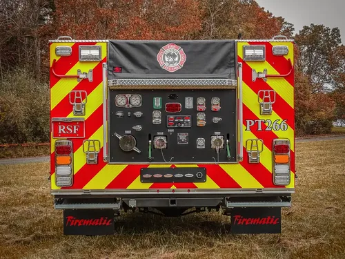 Exterior view of small fire truck showing cab, body compartments, and wheel/tire area.