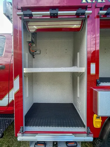 Exterior view of small fire truck showing cab, body compartments, and wheel/tire area.