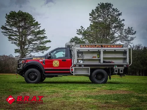 Exterior view of small fire truck showing cab, body compartments, and wheel/tire area.