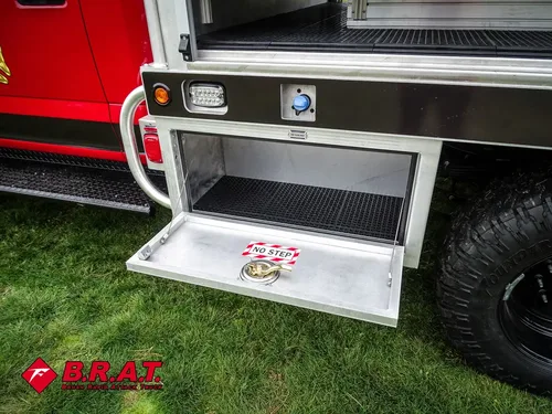 Exterior view of small fire truck showing cab, body compartments, and wheel/tire area.