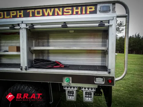 Exterior view of small fire truck showing cab, body compartments, and wheel/tire area.