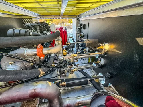 Close-up of pump plumbing and valves inside an open side compartment.