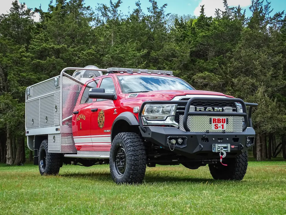 Exterior view of small fire truck showing cab, body compartments, and wheel/tire area.