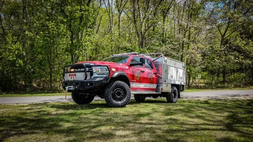Exterior view of small fire truck showing cab, body compartments, and wheel/tire area.