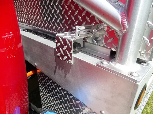 Exterior view of small fire truck showing cab, body compartments, and wheel/tire area.