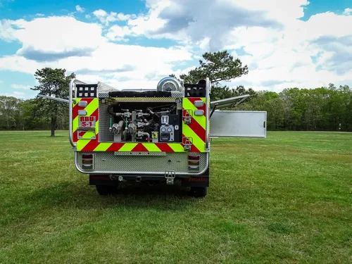 Exterior view of small fire truck showing cab, body compartments, and wheel/tire area.