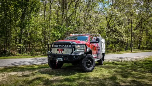 Exterior view of small fire truck showing cab, body compartments, and wheel/tire area.
