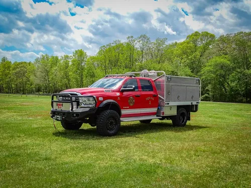 Exterior view of small fire truck showing cab, body compartments, and wheel/tire area.