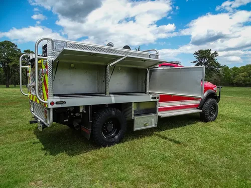 Exterior view of small fire truck showing cab, body compartments, and wheel/tire area.