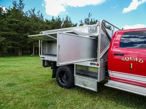 Exterior view of small fire truck showing cab, body compartments, and wheel/tire area.
