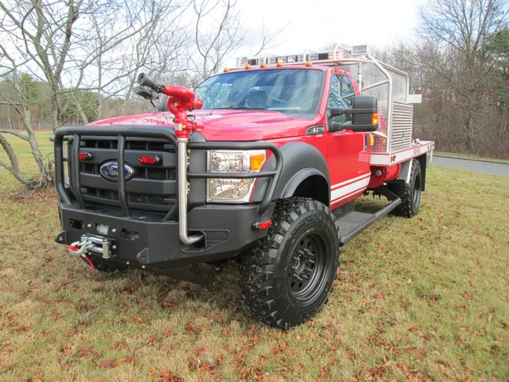 Exterior view of small fire truck showing cab, body compartments, and wheel/tire area.