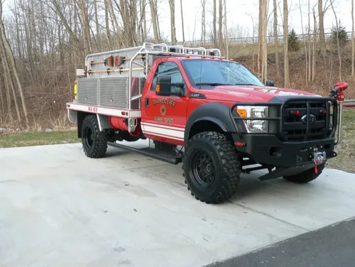 Exterior view of small fire truck showing cab, body compartments, and wheel/tire area.