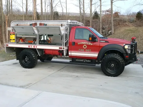 Exterior view of small fire truck showing cab, body compartments, and wheel/tire area.
