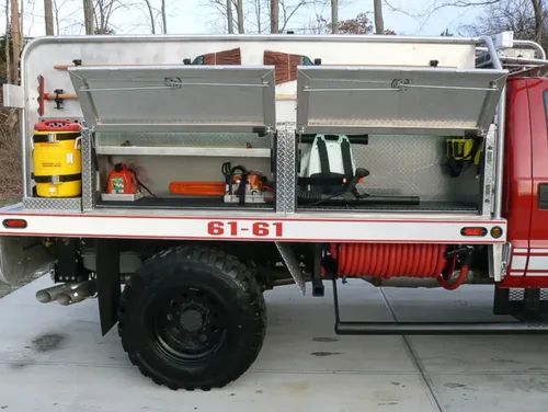Exterior view of small fire truck showing cab, body compartments, and wheel/tire area.