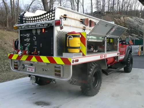 Exterior view of small fire truck showing cab, body compartments, and wheel/tire area.