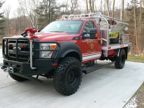 Exterior view of small fire truck showing cab, body compartments, and wheel/tire area.
